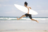サーフボードを持ち砂浜でジャンプする男性