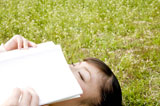芝生に寝転び本を読む女性